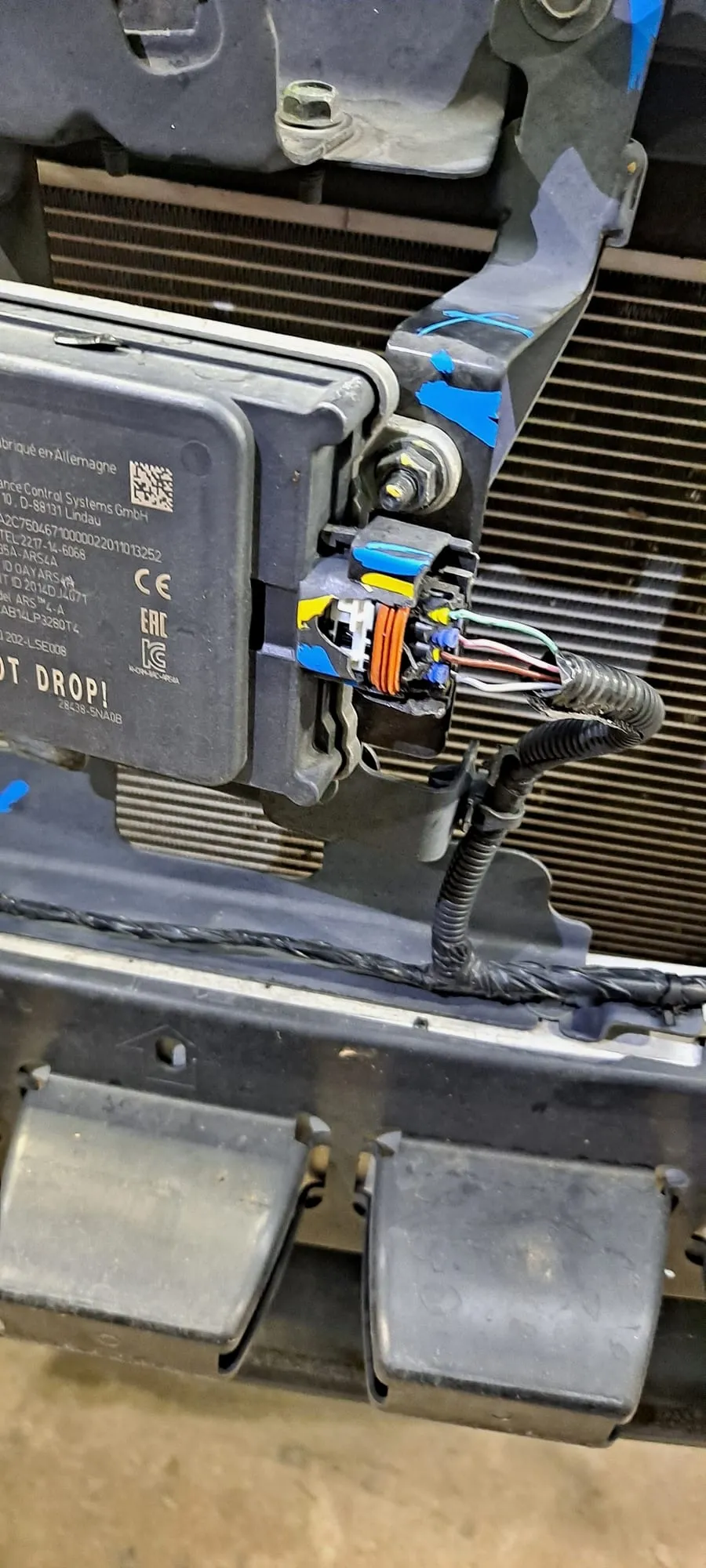 Damaged wiring connector at a bumper-mounted control module, with the coloured wires exposed where the connector body has broken away