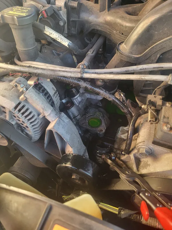 Engine bay of the Explorer with the old thermostat housing off, green coolant sitting in the open port beside the alternator