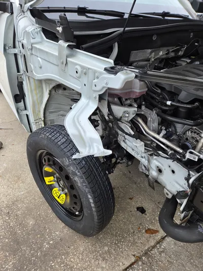 The same car with the front bumper and headlight assembly removed, a narrow spare wheel fitted, and the white inner structure exposed