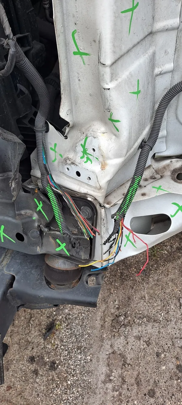Damaged wiring harness in a stripped front corner, the loom opened up to show individual blue, red, yellow and orange wires, with green paint marks on the surrounding structure