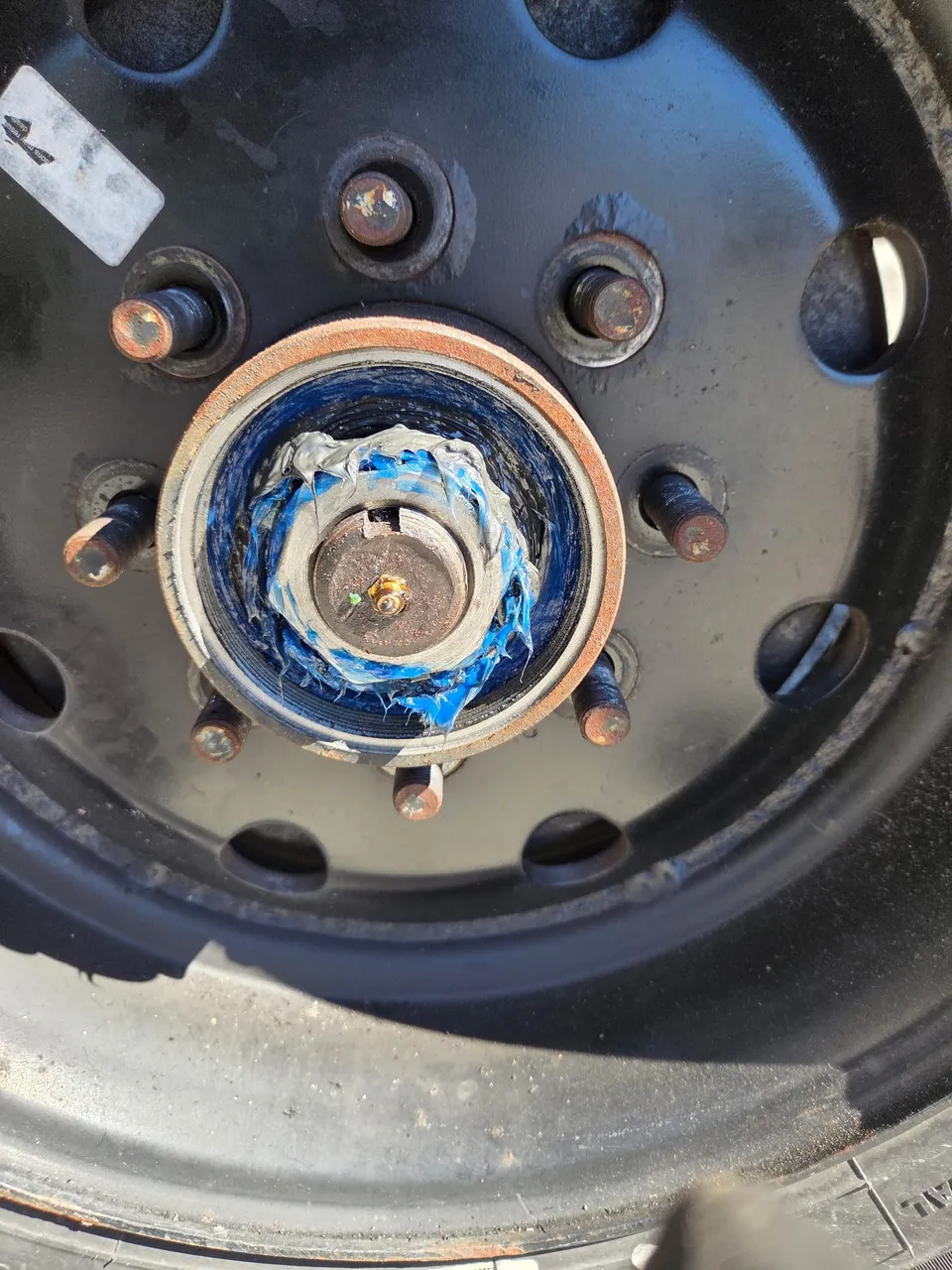 Trailer hub with the grease cap removed, showing the spindle nut and the old grease packed around the bearing inside the black steel wheel