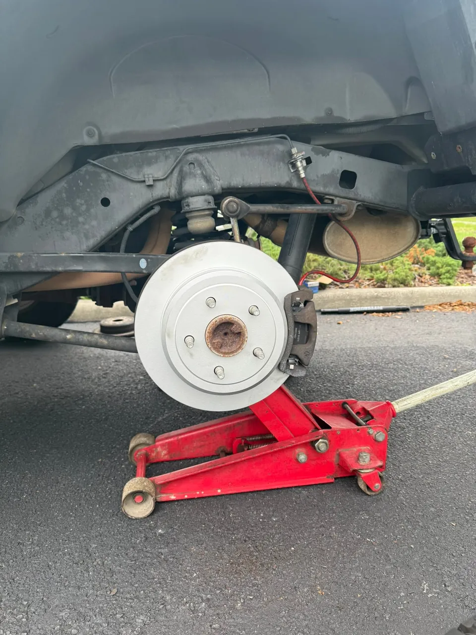 The same rear corner with a new rotor and caliper fitted, the hub clean and the floor jack still under the axle