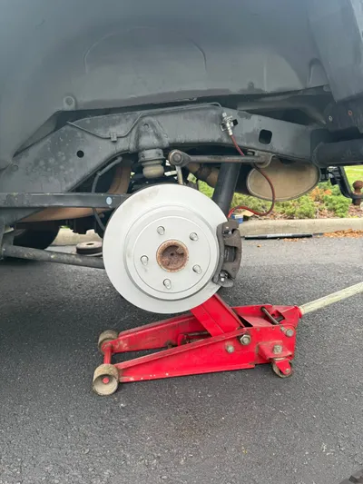 The same rear corner with a new rotor and caliper fitted, the hub clean and the floor jack still under the axle