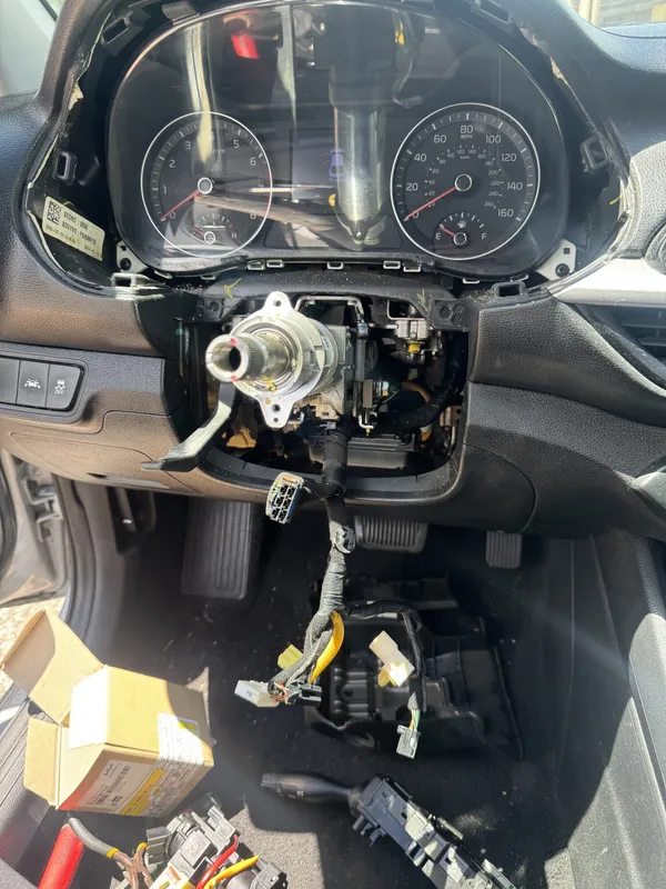 The same column stripped to the shaft with the ignition out, the turn signal and wiper switches on the floor beside an open Kia parts box