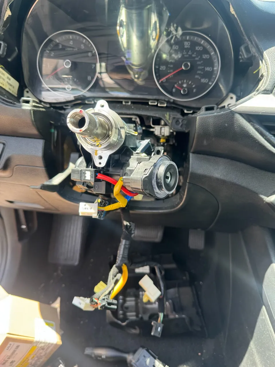 The new ignition fitted to the right side of the steering column, key slot facing out and wiring connected, with the shrouds still off