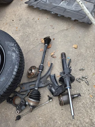 The removed corner laid out on the concrete: strut, driveshaft, lower control arm, steering knuckle, wheel hub and tie rod end, beside the road wheel