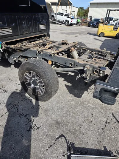 The truck with its bed removed and the rear frame rails exposed, sitting on the ground beside the work area