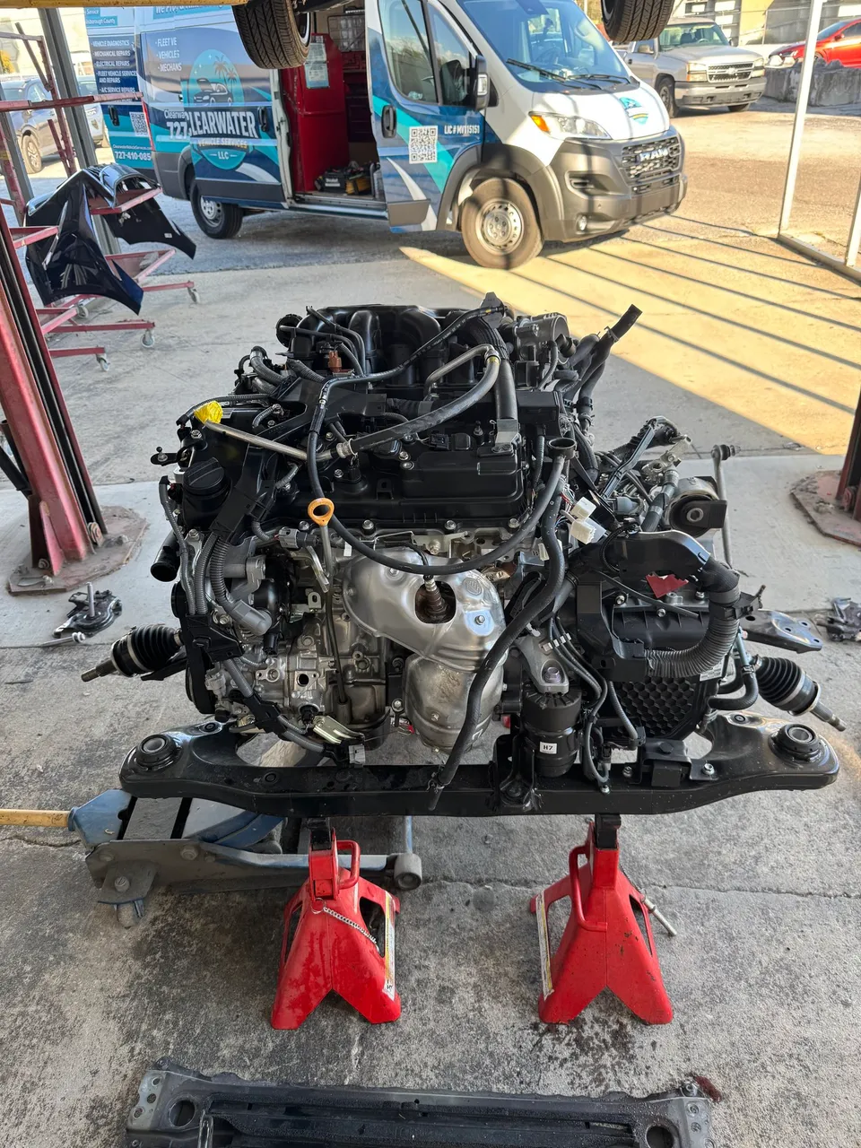 The Lexus engine and transaxle still mounted to its subframe, resting on jack stands beside the Clearwater Vehicle Services van