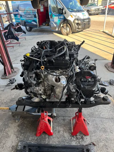 The Lexus engine and transaxle still mounted to its subframe, resting on jack stands beside the Clearwater Vehicle Services van