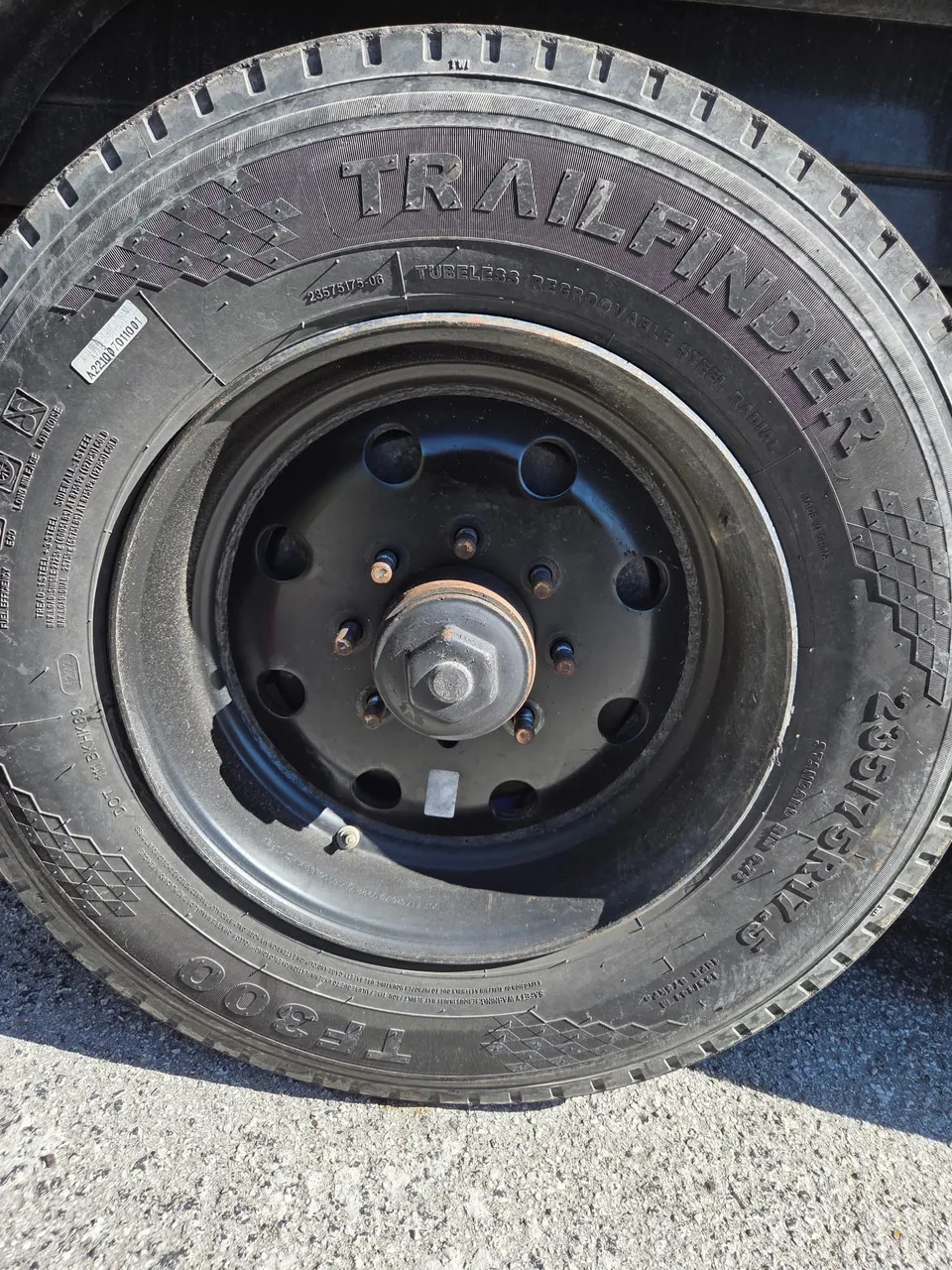 The trailer wheel and tyre refitted to the black steel rim with the lug nuts and grease cap back in place