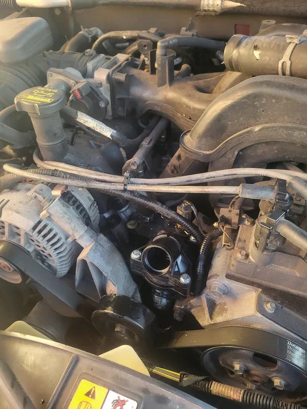 The new thermostat housing bolted to the engine with the drive belt back on its pulleys