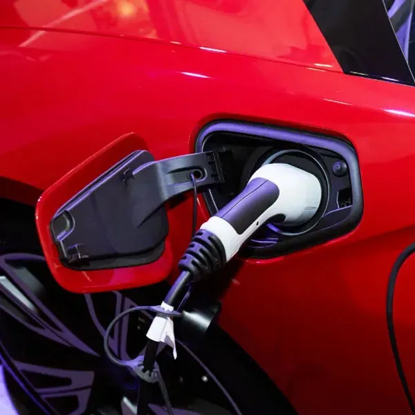 Charging cable plugged into the charge port of an electric vehicle parked outside a home, with the port door open and the status light showing