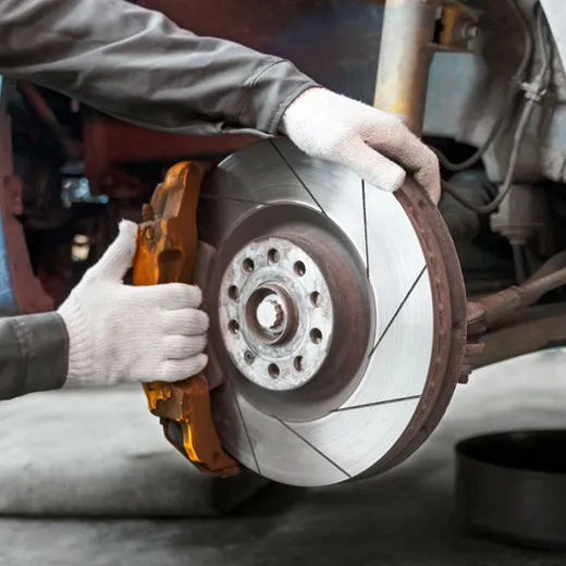 Gloved hands fitting a slotted brake rotor over the hub with the caliper swung clear