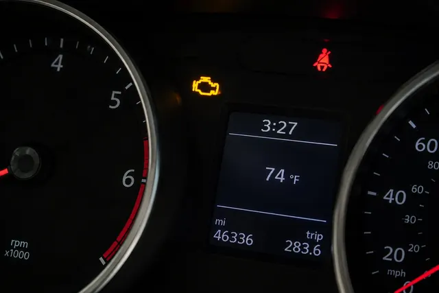 An amber check engine light glowing steady on a dark instrument cluster, between the tachometer and the speedometer, above a trip display reading 46,336 miles