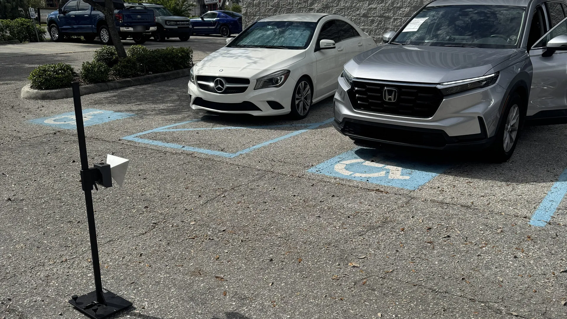 A calibration target on a freestanding stand in a parking lot, set up in front of a silver Honda CR-V, with a white Mercedes sedan parked in the next space