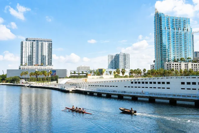 Downtown Tampa across the Hillsborough River, with high-rise towers behind the curved Riverwalk and a rowing crew on the water