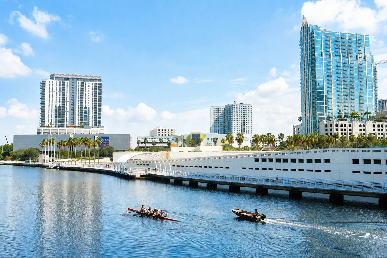 Downtown Tampa across the Hillsborough River, with high-rise towers behind the curved Riverwalk and a rowing crew on the water